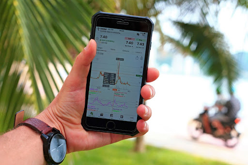 Man holding mobile in his hand looking at trading charts with a beach background