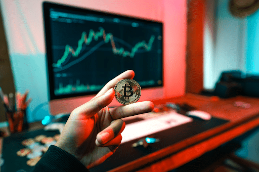 Man holding physical Bitcoin in front of computer screen